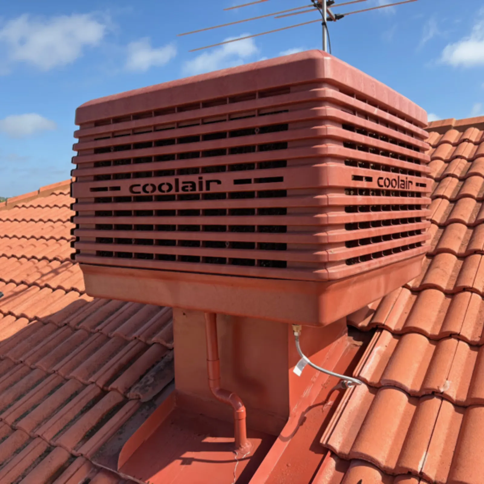 New terracotta-coloured evaporative cooler installed on a tiled roof